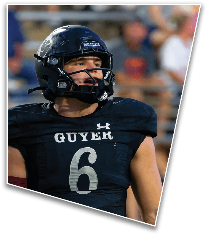 A person wearing a black football uniform with the number six and the word Guyer on the chest is looking to the side while wearing a black helmet with a faceguard. Description generated by AI
