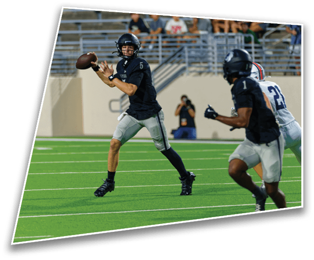 A person wearing a black football uniform and helmet is preparing to throw a football on a green field with empty bleachers in the background. Description generated by AI