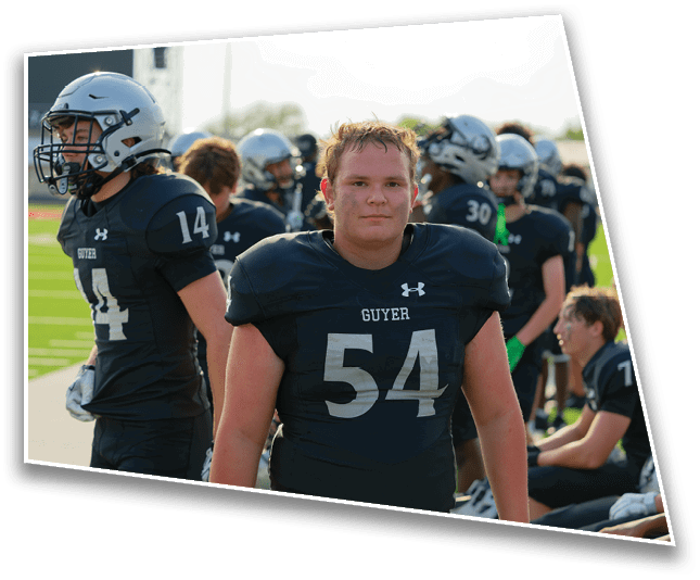 A person wearing a black football uniform with the number 54 stands on a field with teammates in similar uniforms and helmets in the background. Description generated by AI