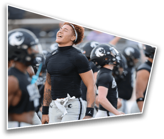 People wearing athletic gear stand on a sports field, with one person in the foreground wearing a tight black shirt and light-colored pants with a white cloth tucked into the waistband. Description generated by AI