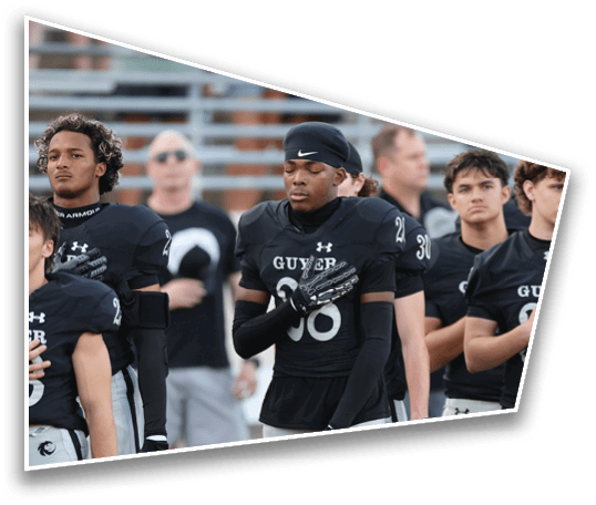 A group of people wearing black football uniforms stand together with one person placing a gloved hand over their chest and eyes closed. Description generated by AI
