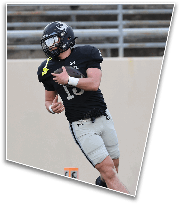 A person wearing a black football uniform and helmet is running on a field while holding a football. Description generated by AI