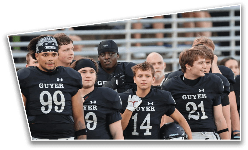 A group of people wearing black sports uniforms are seated in front of metal bleachers with other people standing and sitting in the background. Description generated by AI
