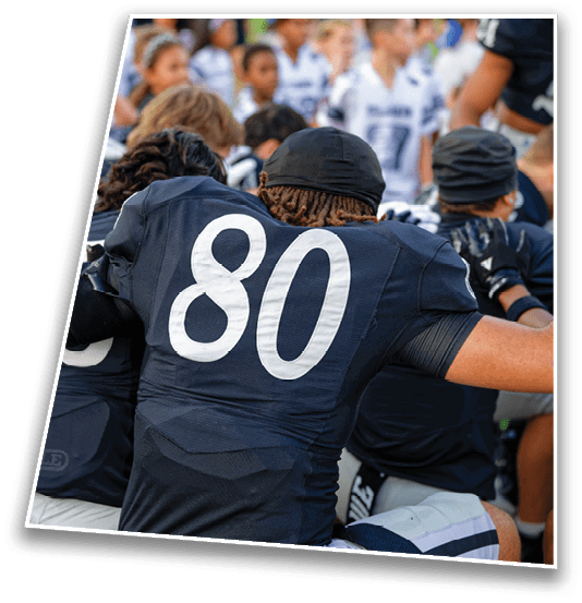 People wearing dark sports jerseys and light pants are kneeling and appear to be engaged in a team huddle or discussion. Description generated by AI
