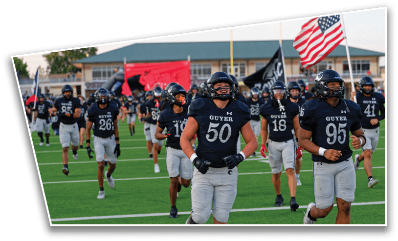 People wearing football uniforms are running on a field with flags waving in the background. Description generated by AI