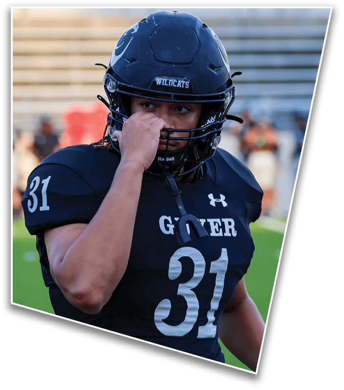 A person wearing a dark football helmet with the word “WILDCATS" on the front is holding their hand near their face while looking to the side. Description generated by AI