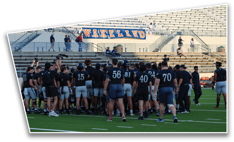 A group of people wearing sports uniforms are gathered on a football field near bleachers with a banner that reads “WAKELAND." Description generated by AI