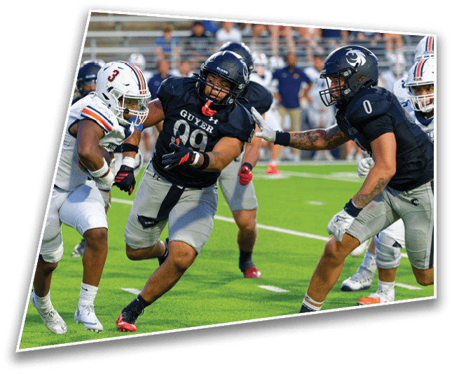 Two people in football uniforms are engaged in a play on a green field with spectators in the background. Description generated by AI