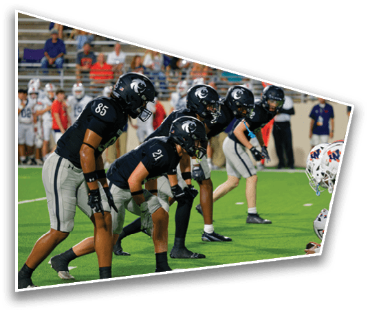 People in football uniforms are lined up on a field in a ready stance, preparing for a play during a game. Description generated by AI