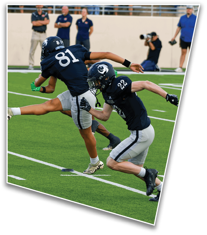 Several people in dark sports uniforms are running on a green football field, with one person in mid-stride extending a leg forward. Description generated by AI