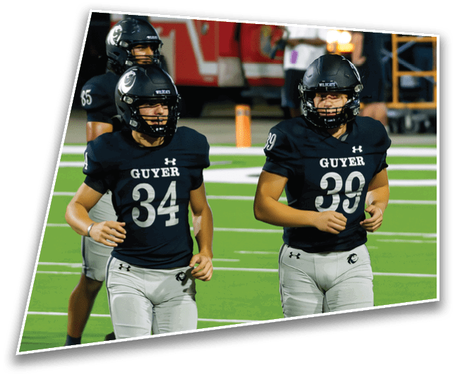 Three people wearing black football helmets and uniforms stand on a field with a red vehicle and a person in the background. Description generated by AI