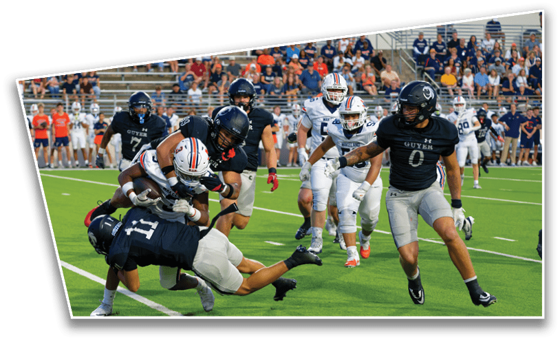 A group of people playing American football on a field with one person in a white uniform being tackled by multiple people in dark uniforms. Description generated by AI