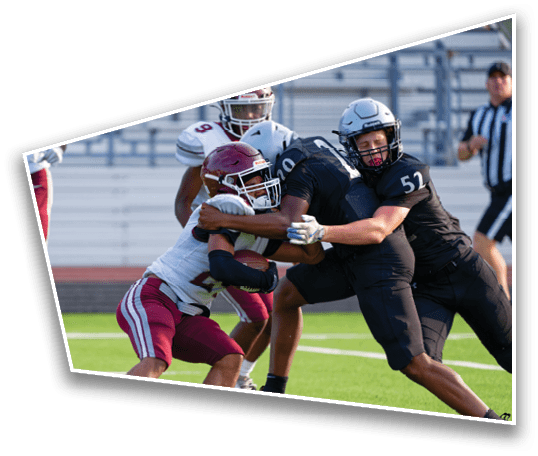 Two people in black uniforms tackle a person in a white and maroon uniform holding a football on a green field during a game. Description generated by AI