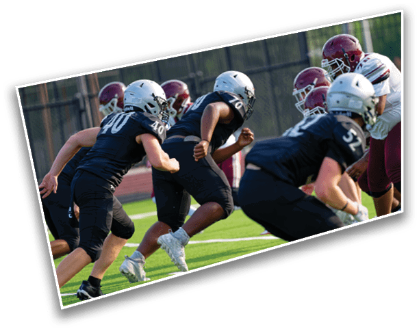 People in football uniforms are lined up on a field preparing for a play during a game. Description generated by AI