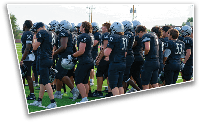 A group of people wearing black football uniforms and helmets are standing together on a green field. Description generated by AI