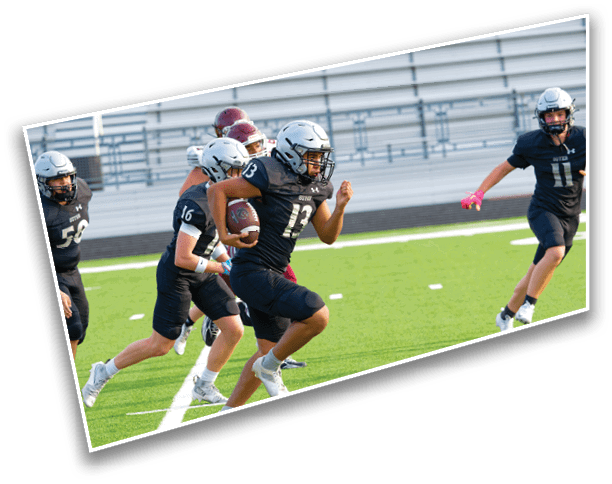 A group of people in football uniforms and helmets are running on a green field with one person holding a football. Description generated by AI