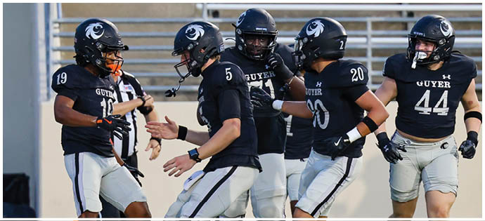 People wearing black sports jerseys and white pants are standing and moving on a green field, appearing to be engaged in a team sport activity. Description generated by AI