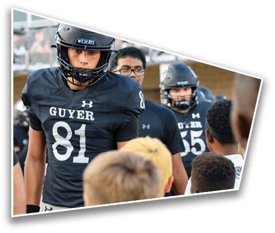People wearing black football uniforms with the word “GUYER" and numbers on them are standing outdoors near children. Description generated by AI
