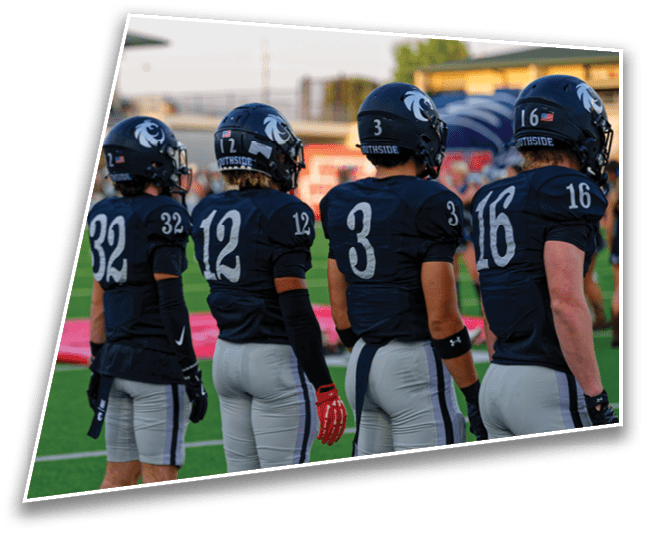 Four people in dark football uniforms and helmets stand side by side on a green field facing away from the camera. Description generated by AI
