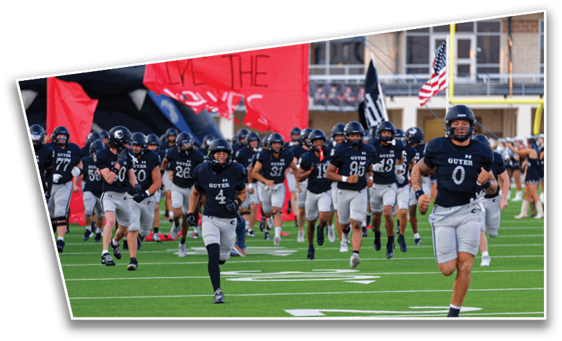 A group of people wearing football uniforms with helmets are running onto a field, some carrying flags. Description generated by AI