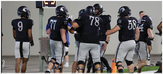 Several people wearing sports uniforms and knee braces are standing on a field near a sideline marker. Description generated by AI