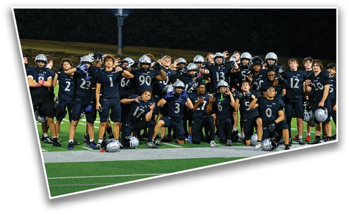 A group of people wearing dark sports uniforms and helmets are posing together on a football field at night. Description generated by AI