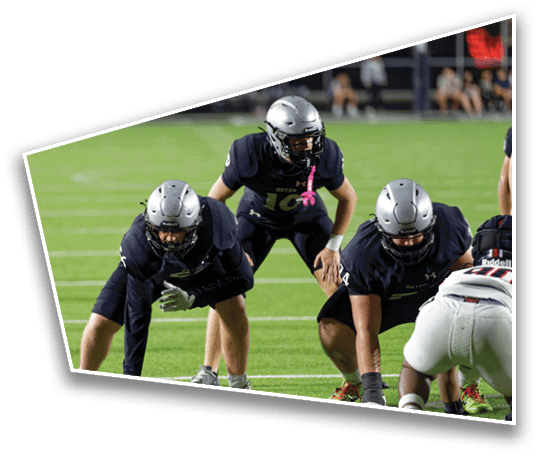 Two people in football gear are positioned on a field, one bent over facing away and the other crouched facing forward, ready for a play. Description generated by AI