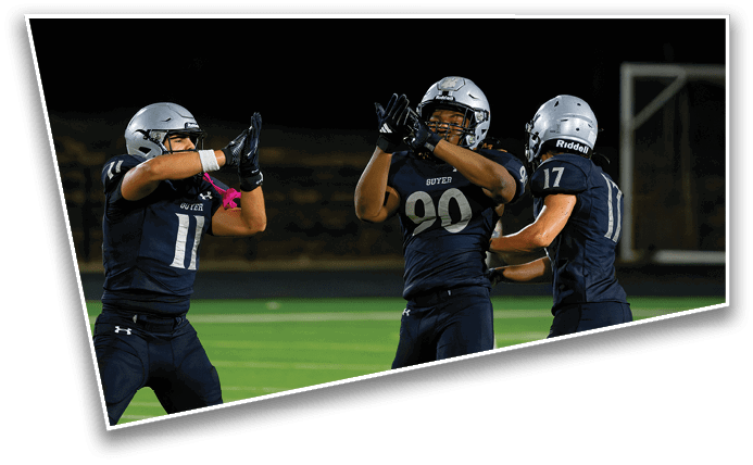 Three people wearing dark football uniforms and helmets are celebrating on a football field at night. Description generated by AI