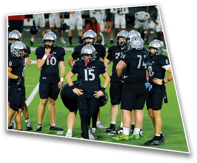 A group of people wearing black sports uniforms and helmets are standing on a green field, with one person in the center standing confidently with hands on hips. Description generated by AI
