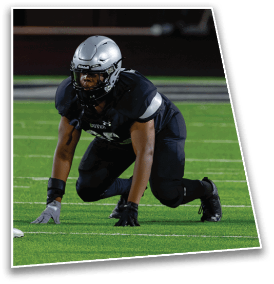 Two people in football uniforms are positioned on a field facing each other, one in a crouched stance and the other bent forward. Description generated by AI
