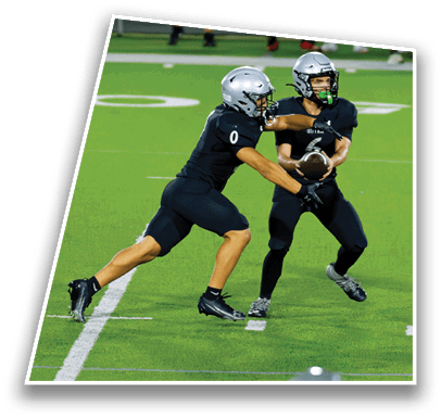 Two people in black sports uniforms and helmets are playing football on a green field, with one person handing off the ball to the other. Description generated by AI