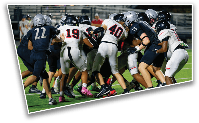 People wearing sports uniforms and cleats are engaged in a close physical play on a grassy field, likely during a football game. Description generated by AI