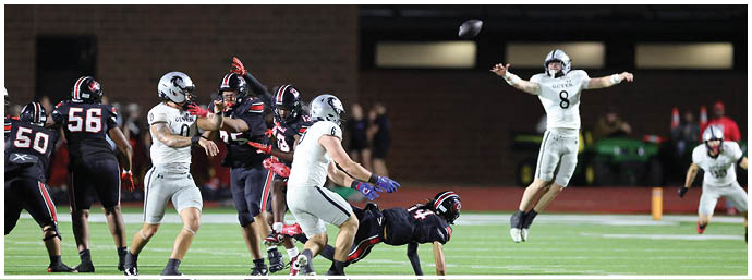 A group of people in football uniforms are actively playing on a field with one person in white jumping and throwing a football. Description generated by AI