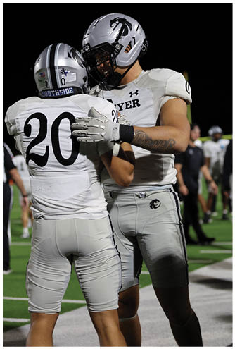 Two people in white football uniforms are embracing on a field during a game. Description generated by AI