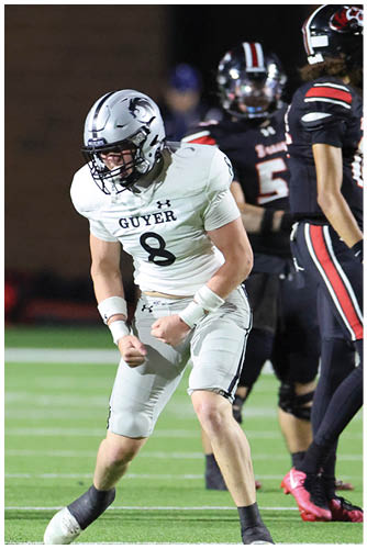 A person in a white football uniform with the number 8 is celebrating on a football field while two people in black uniforms stand nearby. Description generated by AI