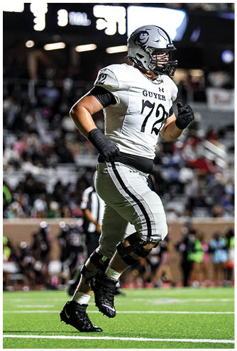 A person wearing a football uniform with the number 72 and the word “GUYER" is running on a football field during a game. Description generated by AI