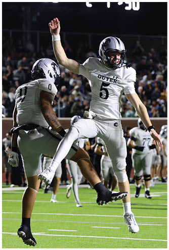 Two football players in white uniforms jump in celebration on a field during a night game. Description generated by AI