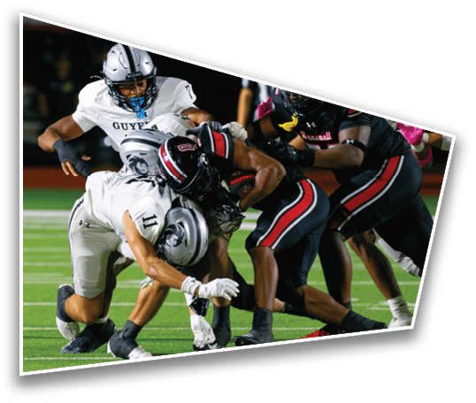 Several people in football uniforms are engaged in a tackle on a green field during a game. Description generated by AI