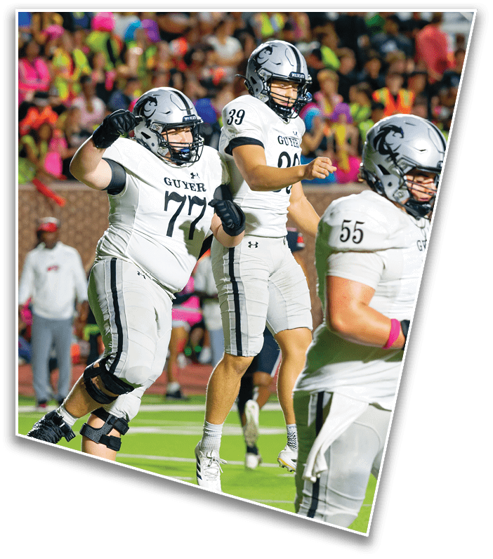 Two football players in white uniforms and helmets are on the field with a blurred crowd in the background. Description generated by AI