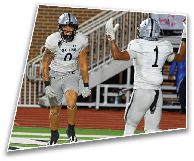 Two people in football uniforms are on a field near the end zone, with one person running and the other raising an arm. Description generated by AI