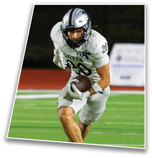A person wearing a white football uniform with the word “GUYER" and number 30 is running with a football on a field at night. Description generated by AI