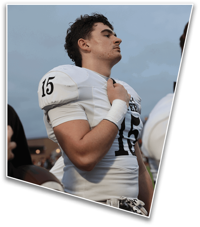 A person wearing a white football uniform with the number 15 stands with a hand on their chest against a cloudy sky background. Description generated by AI