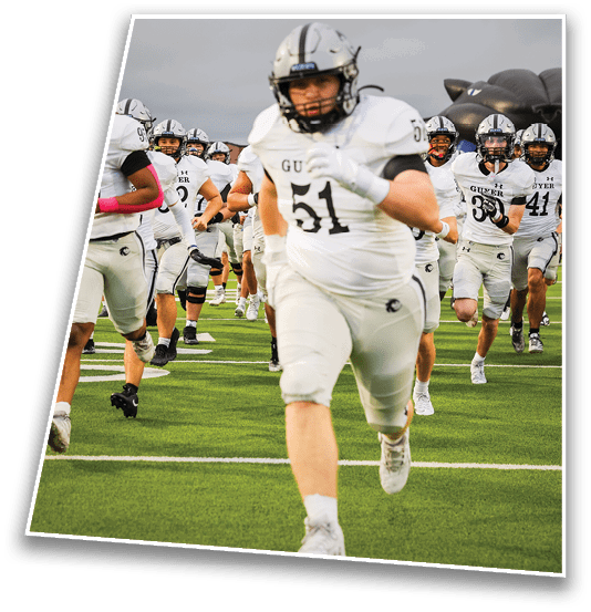 A group of people wearing white football uniforms with helmets are running on a green field toward the camera. Description generated by AI