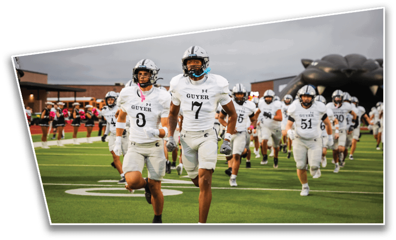 People in sports uniforms are running on a football field with yard lines visible. Description generated by AI
