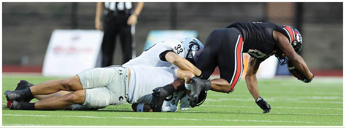 A close-up view of a green sports field with white yard lines and a few people standing in the background. Description generated by AI