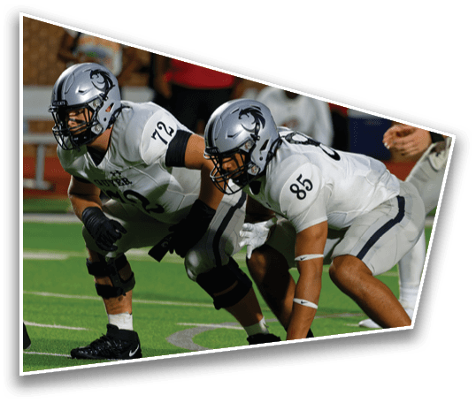 Two people in football uniforms and helmets are crouched in a ready position on a football field. Description generated by AI