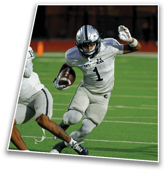 A person wearing a silver helmet and white football uniform with the number one is running on a green field while holding a football. Description generated by AI