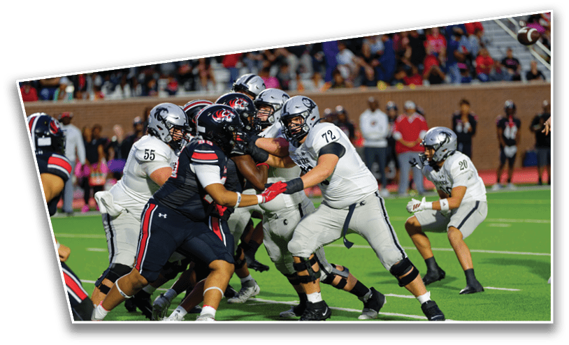 Several football players in helmets and uniforms are engaged in a close physical play on a field with spectators in the background. Description generated by AI