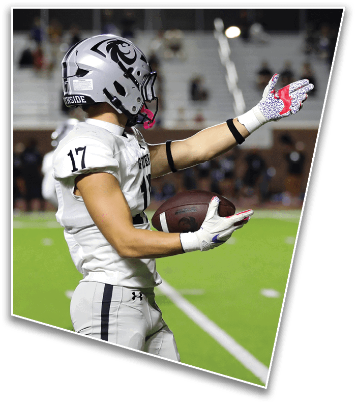 A person wearing patterned gloves is catching a football on a green field with blurred spectators in the background. Description generated by AI