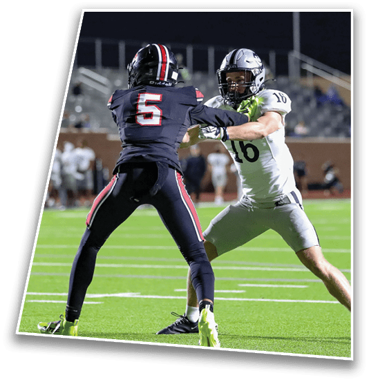 A person wearing a black football uniform with the number five is standing on a green field facing another player during a game. Description generated by AI